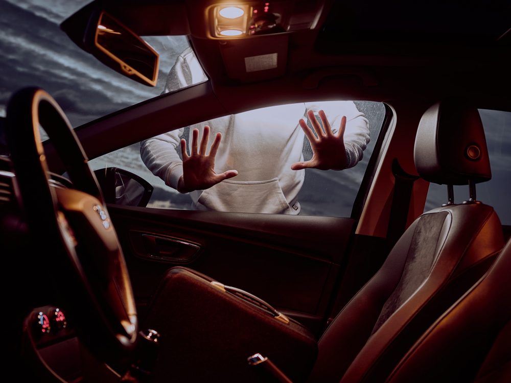 person in white sweater with their hands on a car's side window as if about to attempt to steal it