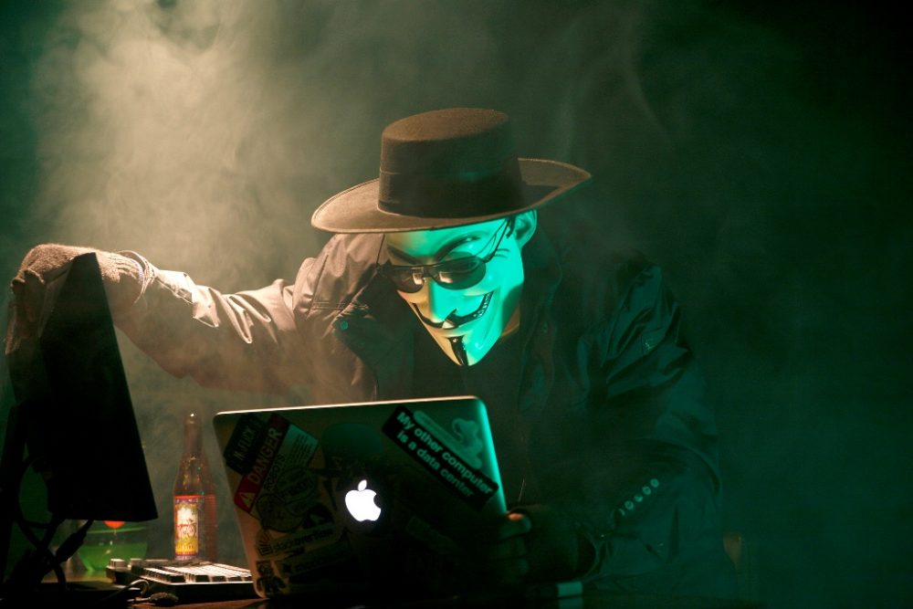 An exaggerated portrayal of a hacker hard at work on a laptop and desktop computer.