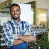 Cheerful handsome bearded Black man factory worker in gloves crossing arms on chest