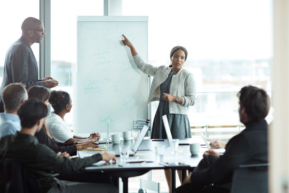 Woman presenting to team of office executives around table