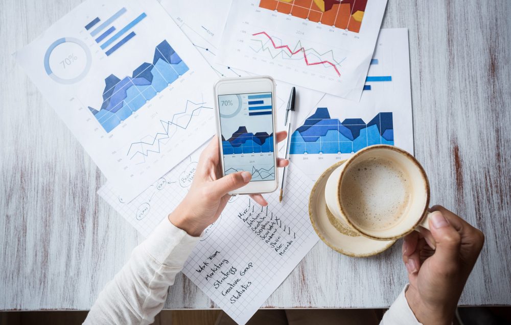 Graphs and charts on paper on desk with worker looking at phone