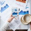 Graphs and charts on paper on desk with worker looking at phone