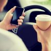 man using phone and holding coffee while driving car