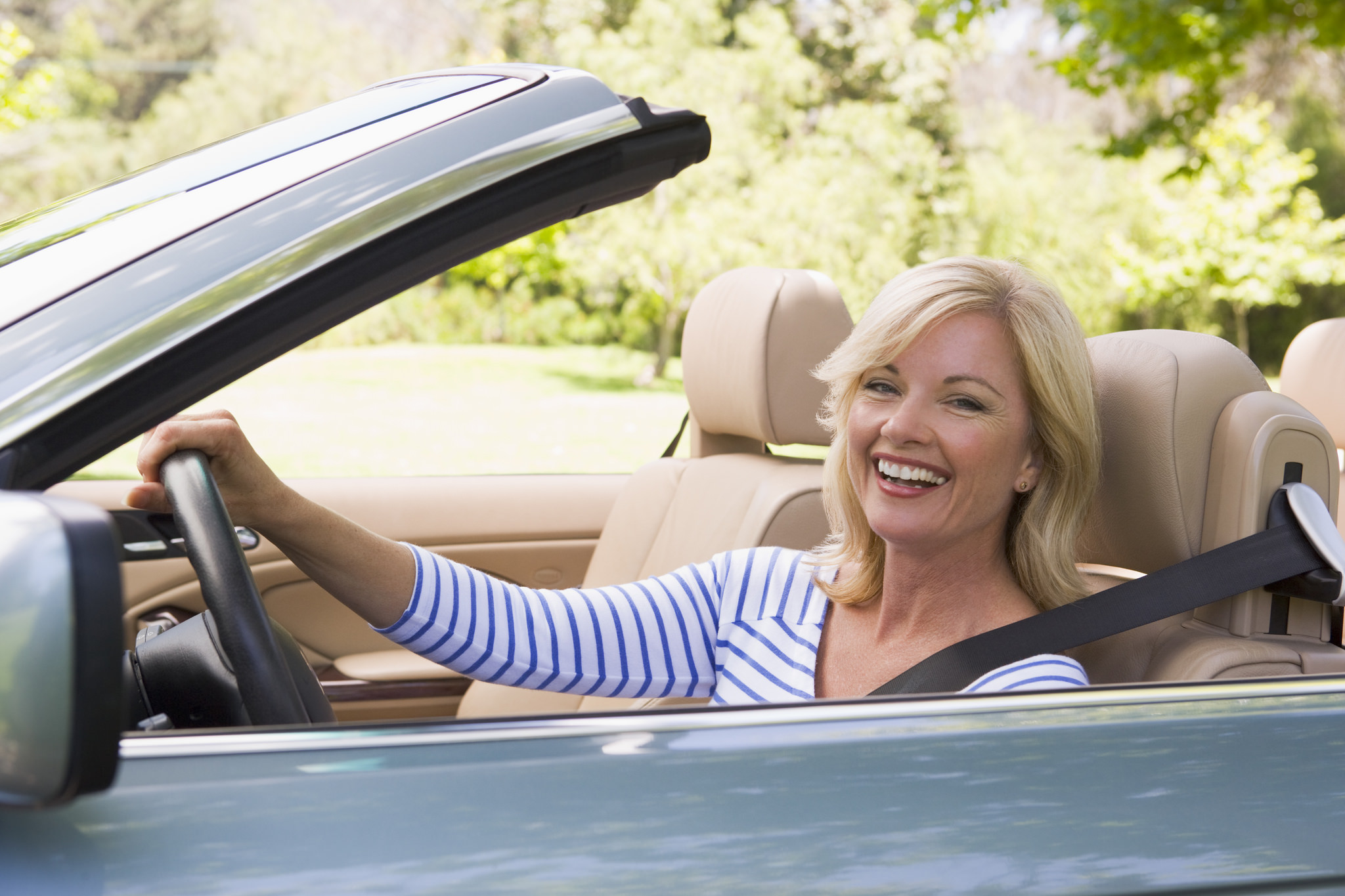 Happy blonde woman with flowing hair waving in a convertible - wide 2
