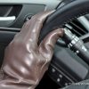 brown leather driving gloves on car steering wheel left hand