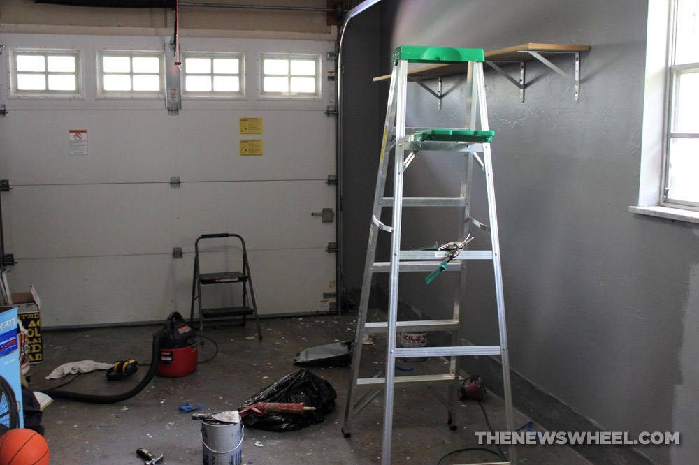 Interior of a garage with a  ladder, step-ladder, shop-vac, paint, scraper, boxes, and a basketball