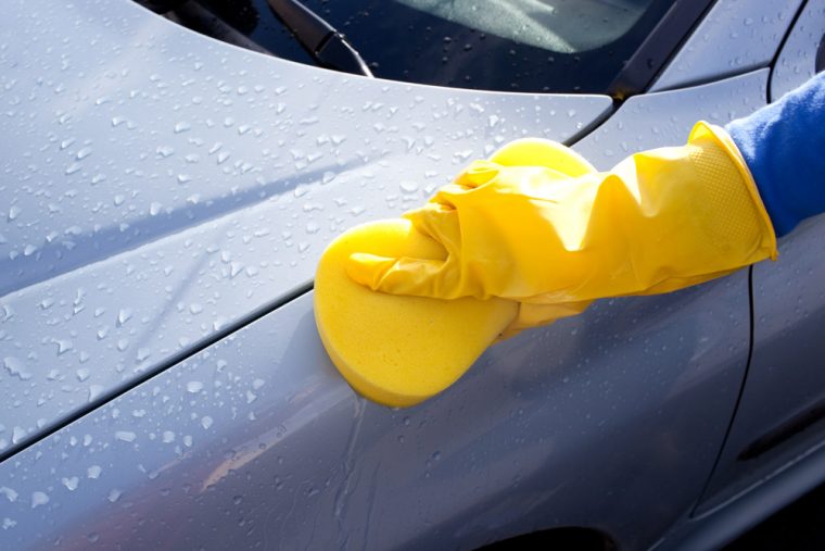 Rubber-gloved hand washing a car using a yellow sponge