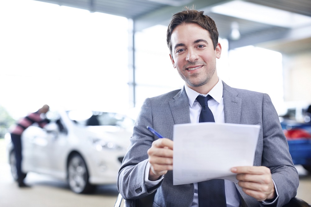 male car salesman holding used car paperwork