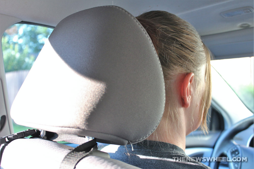Photo of a car driver's seat grey fabric headrest and the back of the driver's head taken from rear sear