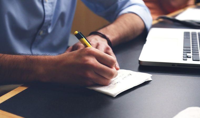 man using computer and taking notes