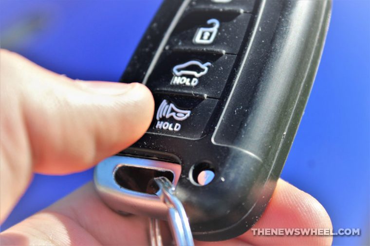 thumb about to press the horn button on a black car key fob