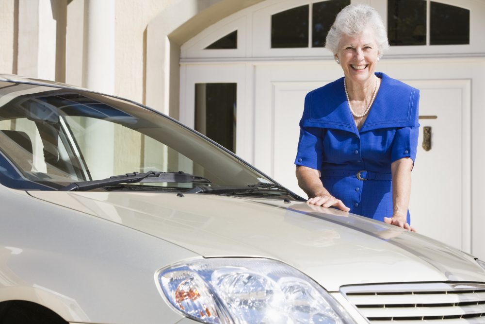 Elderly empty nester woman standing near used car after purchasing