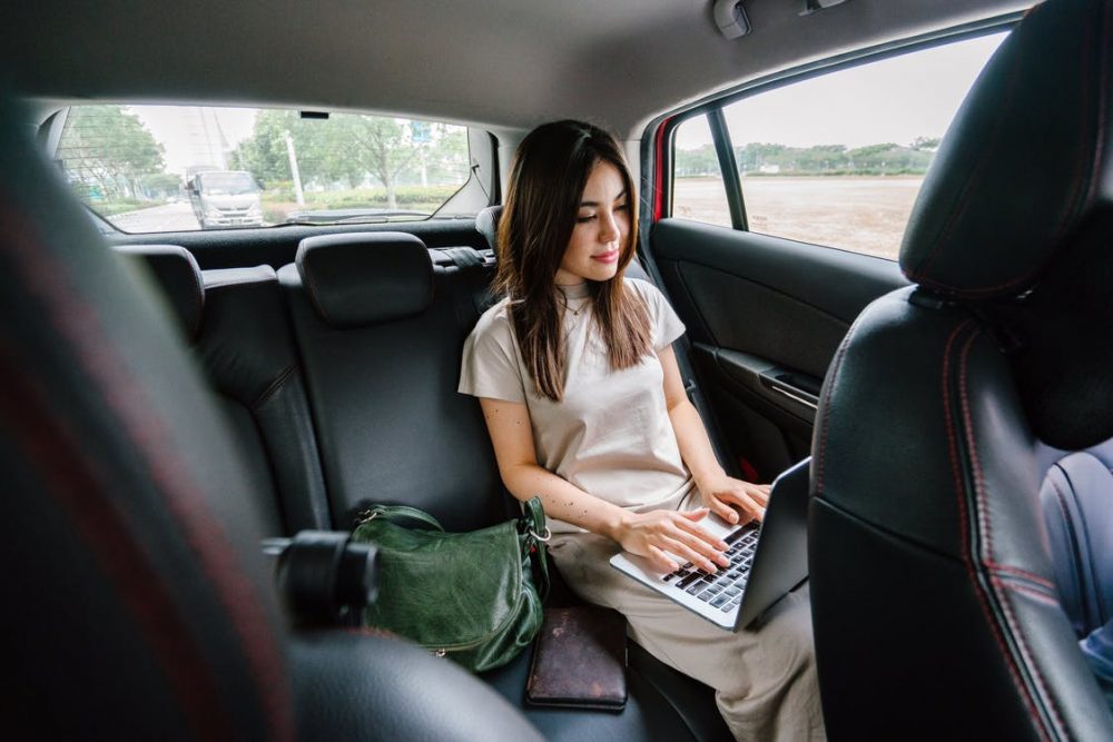 woman working on a laptop in the rear seat of a car