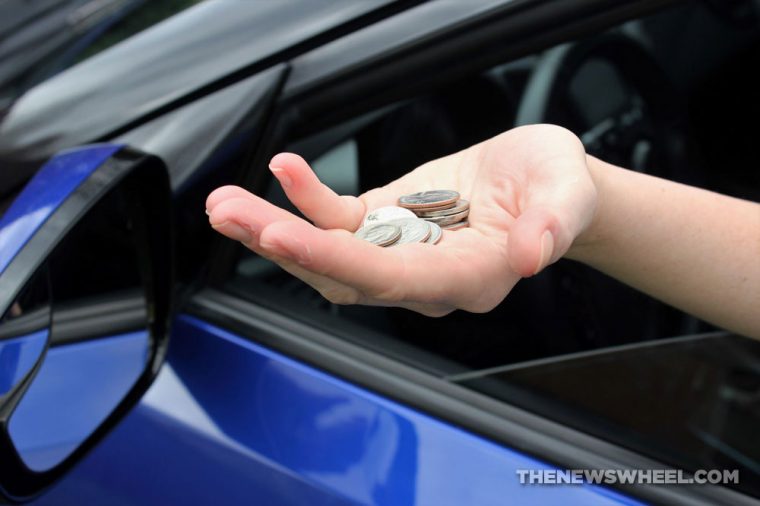 Driver's hand reaching out of a car window with a collection of coins in their palm to pay a toll