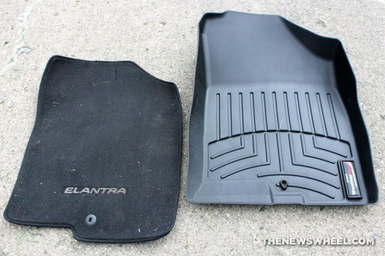 A Hyundai Elantra carpet floor mat next to a Weathertech Floorliner rubber car mat on a concrete surface