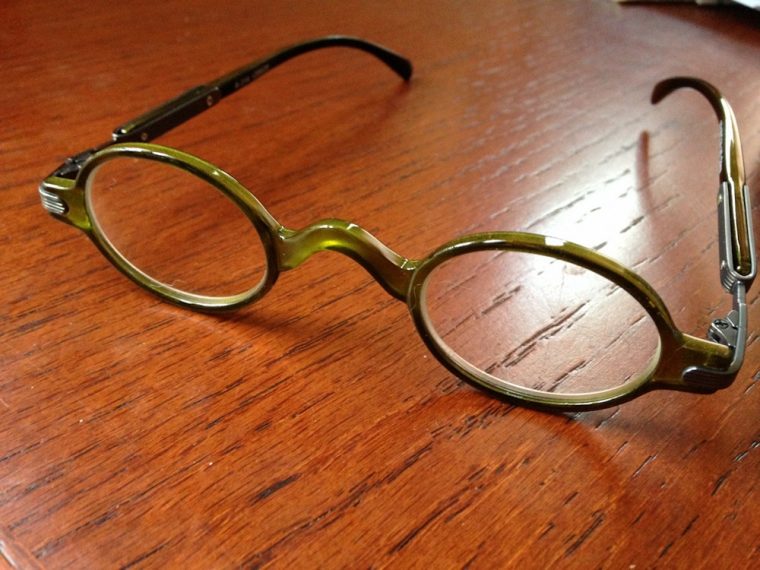 A pair of round-rimmed glasses sitting on a wooden table.