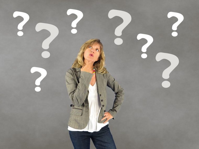 Stock image of woman looking thoughtful. Grey background with white question marks photoshopped on.