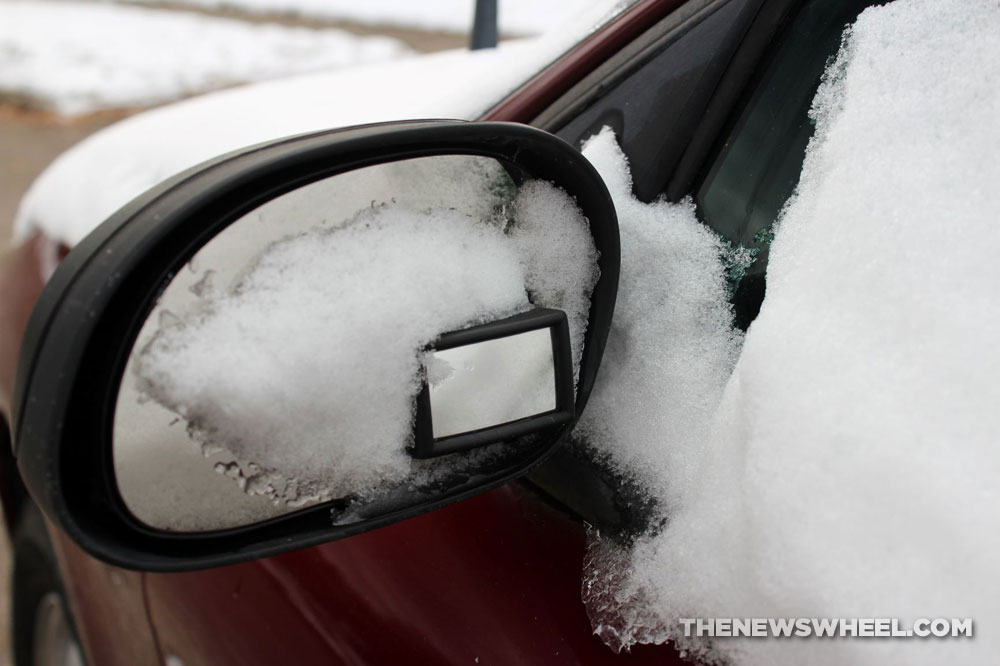 Snow-covered side-view mirror on car in winter 