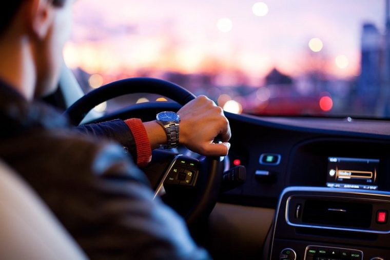 driver wearing a fancy watch sitting behind the wheel of a car with the sunset in the background