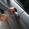 Person using a screwdriver to break into a grey vehicle