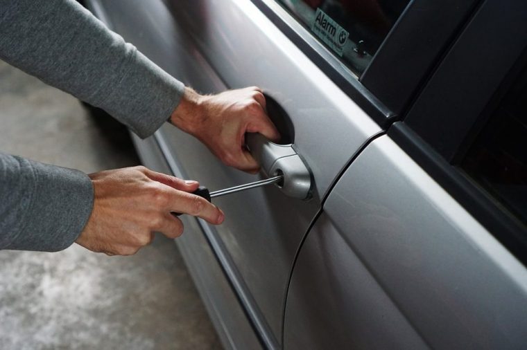 Person using a screwdriver to break into a grey vehicle