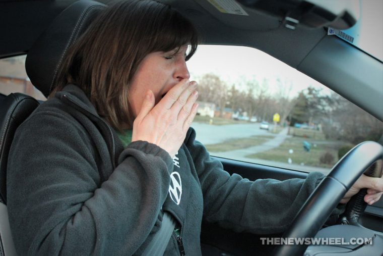 female driver yawning with her eyes closed while behind the wheel