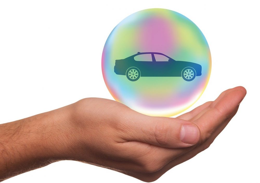 A hand holding a iridescent globe with a car silhouette 