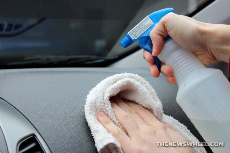 Person spraying cleaning solution onto a car dashboard and holding a towel