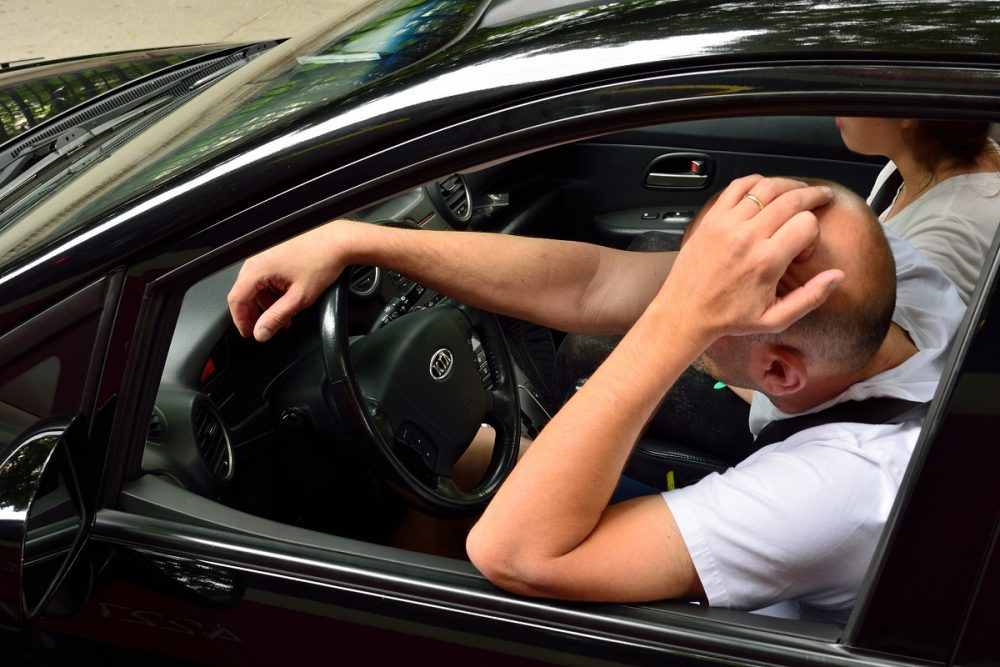 Male driver resting one hand on the wheel and one hand on his head as if drowsy