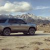 Sideview of a silvery grey 2021 Chevrolet Tahoe Z71 SUV in a desert landscape with mountains in the distance under a partly cloudy blue sky