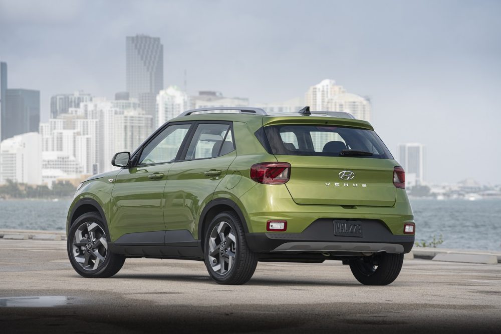 Rear side view of green Hyundai Venue parked on waterfront with city skyline in background