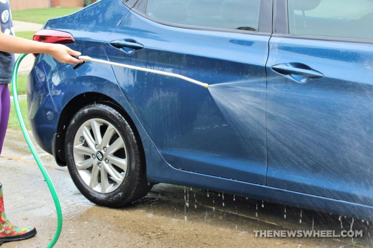 Person washing a blue car using a pressure washer