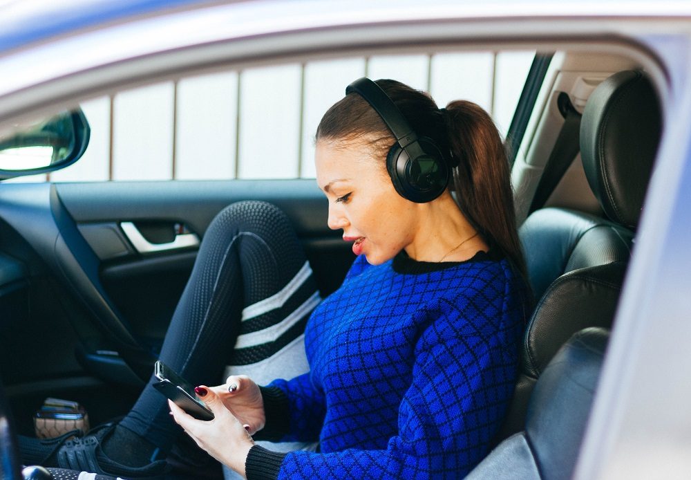 Woman sits in front passenger seat of a car with her knee up