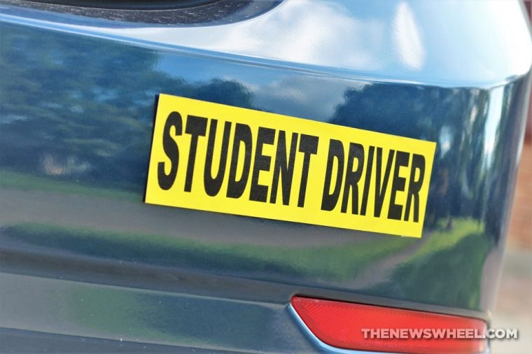 yellow student driver sticker with black writing on the rear bumper of a car
