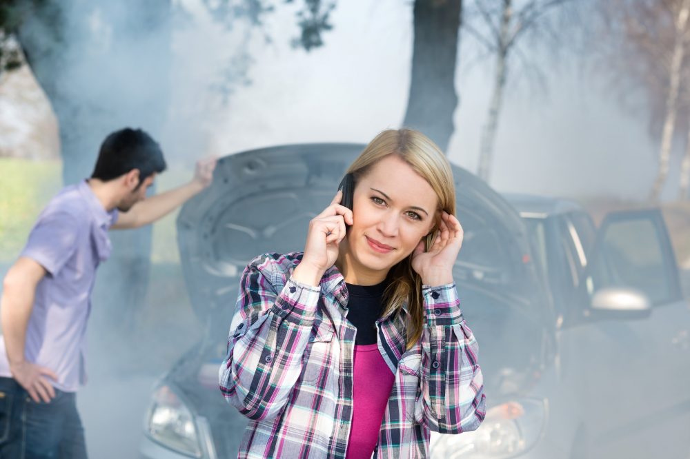 A person is on the phone in front of a broken-down car