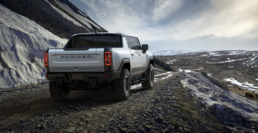 Rear side view of 2022 GMC Hummer EV on mountain overlook next to snowy slopes 