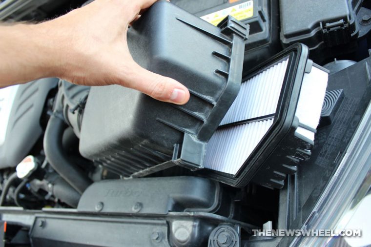 Hand removing cover in the engine bay to reveal a car engine air filter