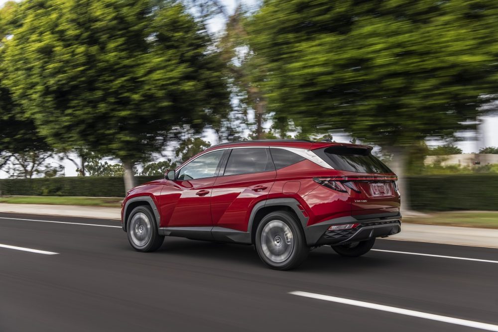 Rear side view of red 2022 Hyundai Tucson driving down road with trees in the background