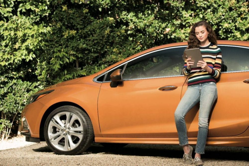 A person leaning against a Chevy Cruze while looking at a tablet