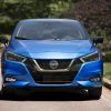 Front view of blue 2021 Nissan Versa parked on pavement with trees in the background