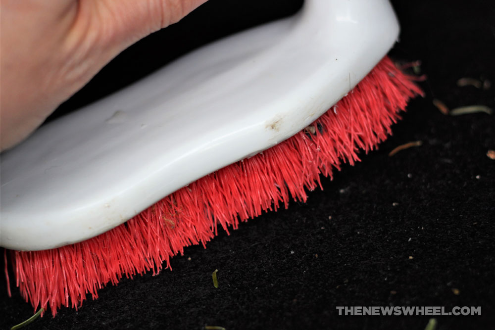 Red and white carpet brush being used on a car's floor mat or seat upholstery