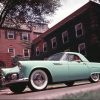 A green 1955 Ford Thunderbird with a woman at the wheel