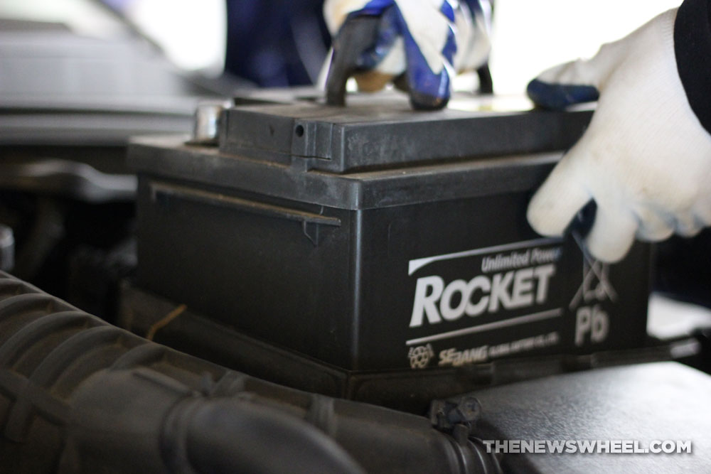 Gloved hand holding a car battery within a car engine