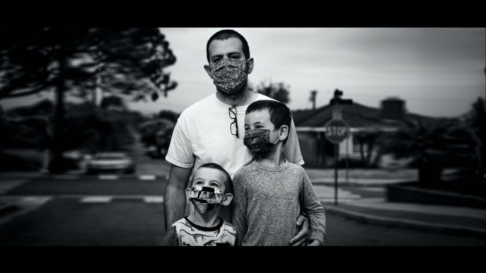 Ford #FinishStrong TV commercial narrated by Bryan Cranston and directed by Peter Berg. This screenshot shows a father and his two children wearing a mask in black and white.