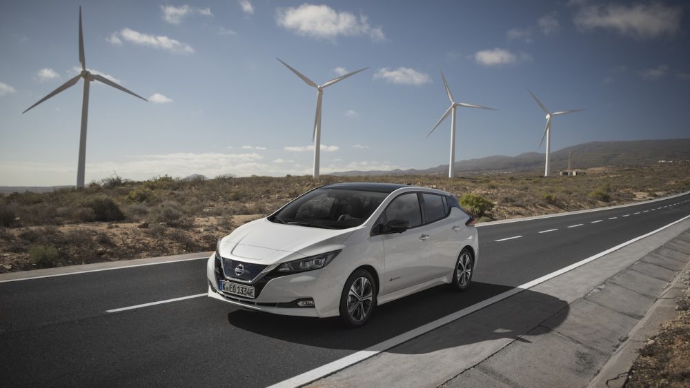 White Nissan Leaf driving on highway with windmills in the background