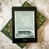 Driving While Black cover displayed on a Kindle Paperwhite as it sits on a green book and a marble counter