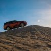 Side and distant view of a red 2022 Nissan Pathfinder driving up a sandy hill