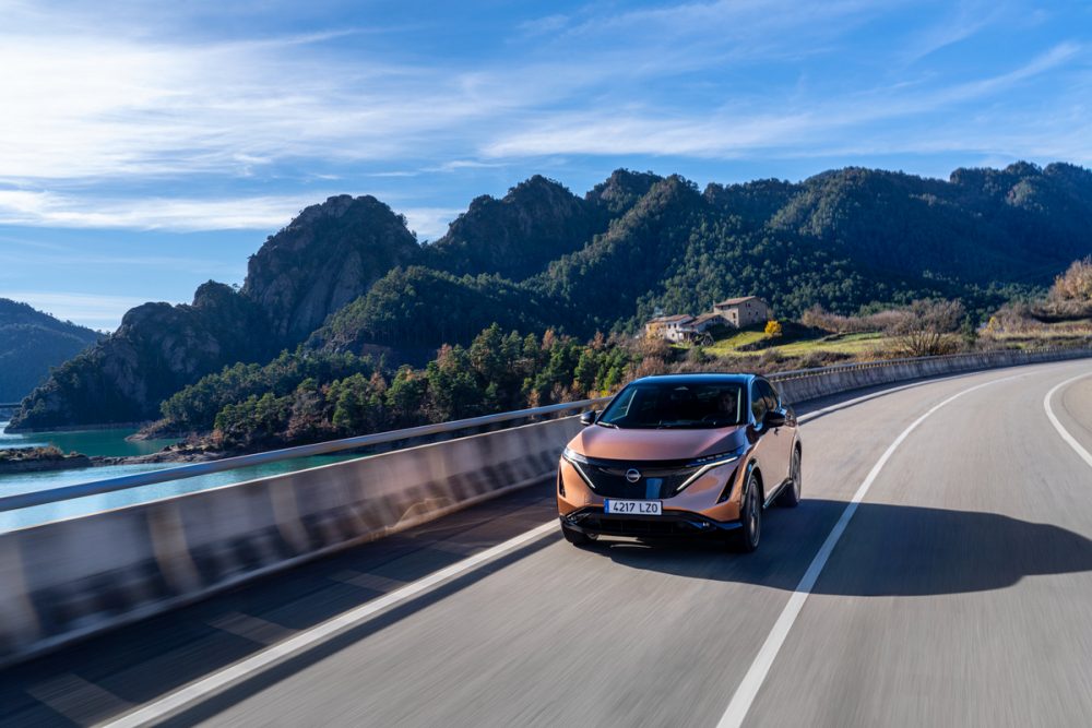 Nissan Ariya driving on mountain road by lake