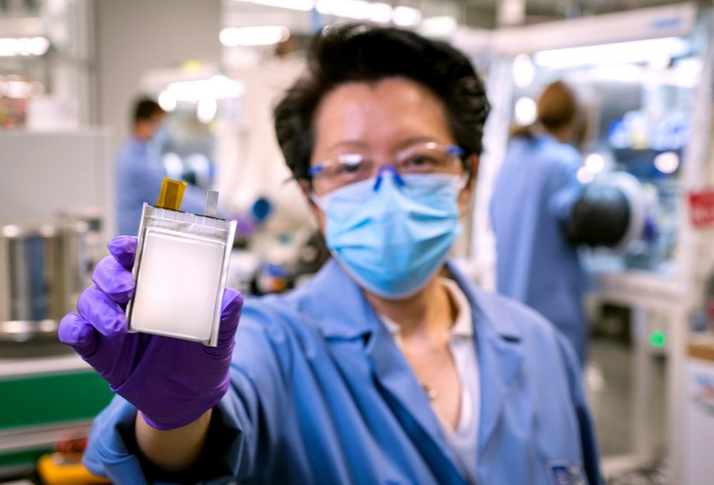 Woman in lab coat and mask holding new GM lithium metal battery