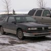 a 1987 Oldsmobile Cutlass in a snowing parking lot, reminiscent of a scene from 'Fargo"